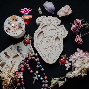 wooden heart art therapy project surrounded by dried flowers, jewelry, and crystals