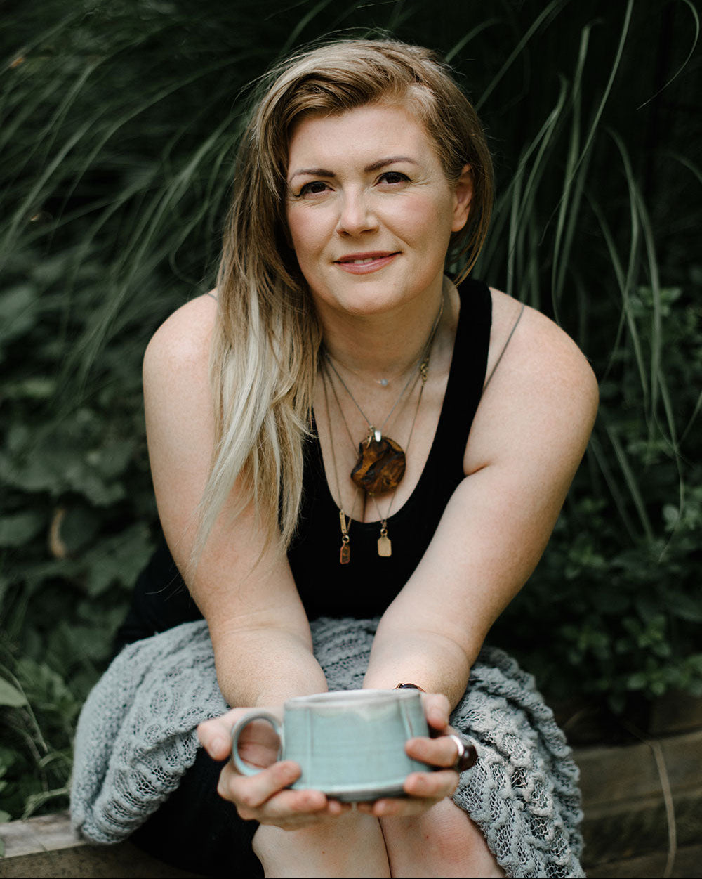 Pamela Scharback local London Ontario artist and painter. Sitting outdoors on the edge of her garden in Old East Village holding a cup of coffee. Pamela specializes in floral, portrait, landscape, mural and chalkboard painting.