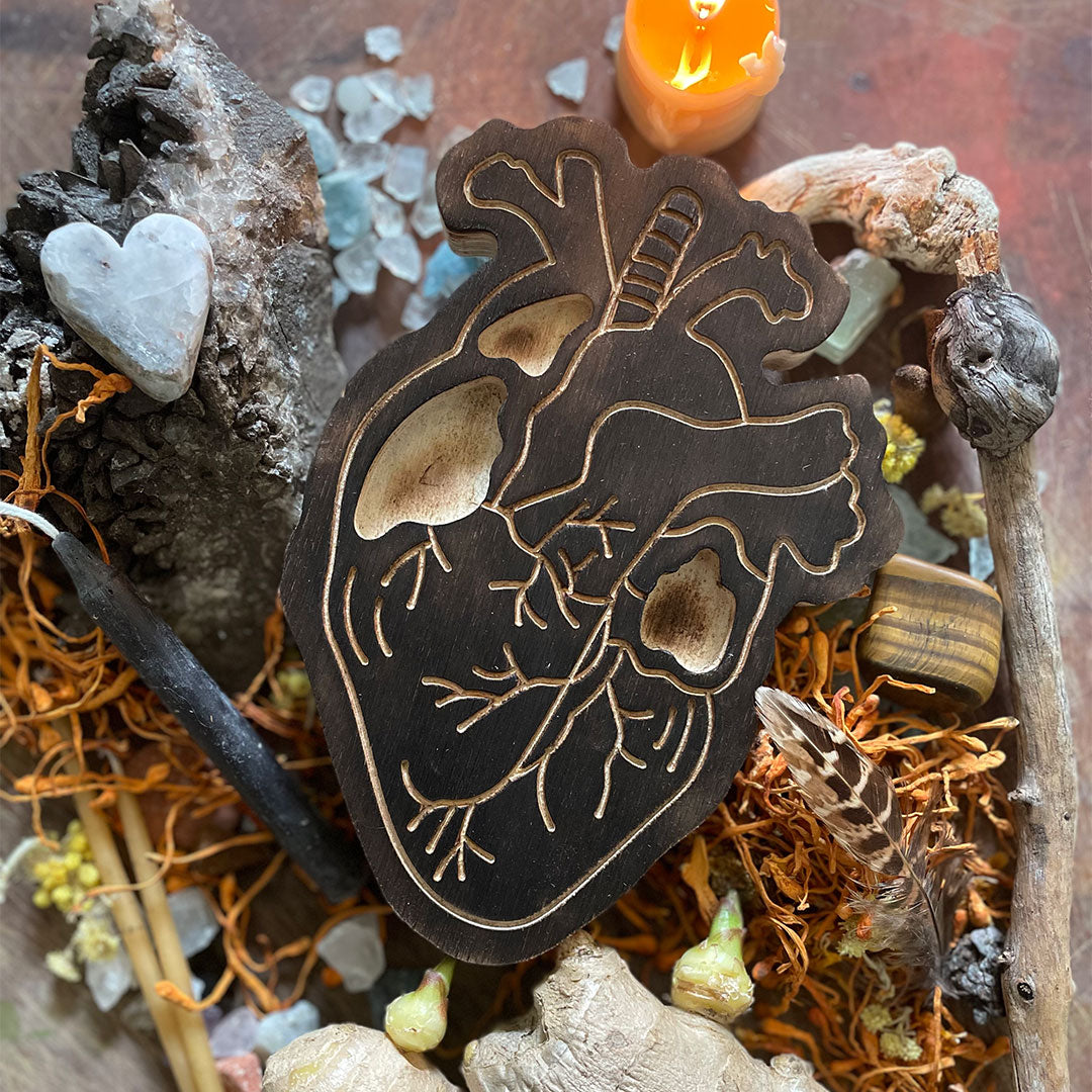 smudged wooden heart art therapy project surrounded by dried flowers, jewelry, and crystals