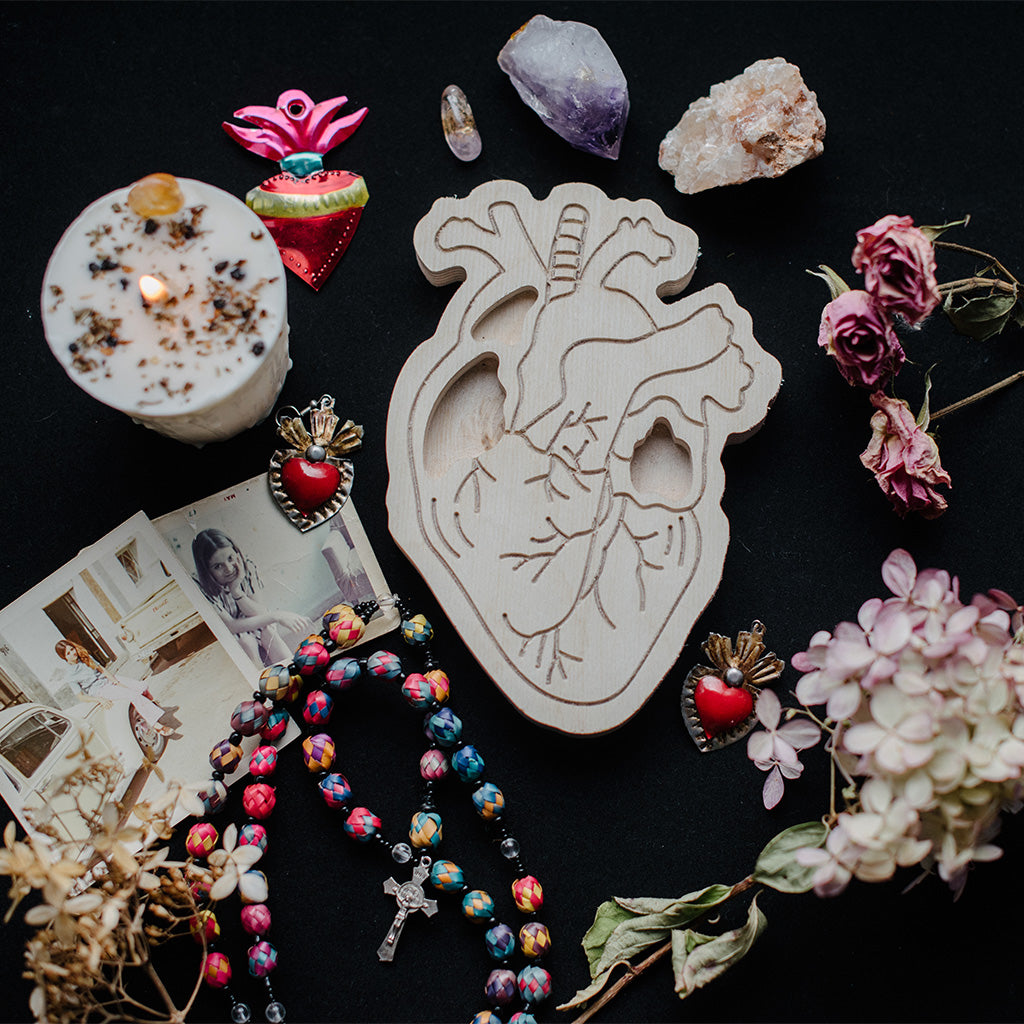 wooden heart art therapy project surrounded by dried flowers, jewelry, and crystals